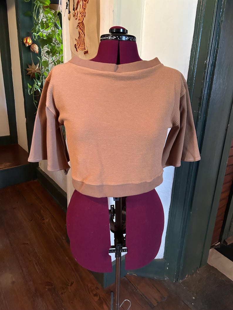 May include: A brown waffle knit cropped top with a boat neck and 3/4 sleeves. The top is on a dress form.