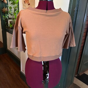 May include: A brown waffle knit cropped top with a boat neck and short sleeves. The top is on a dress form.