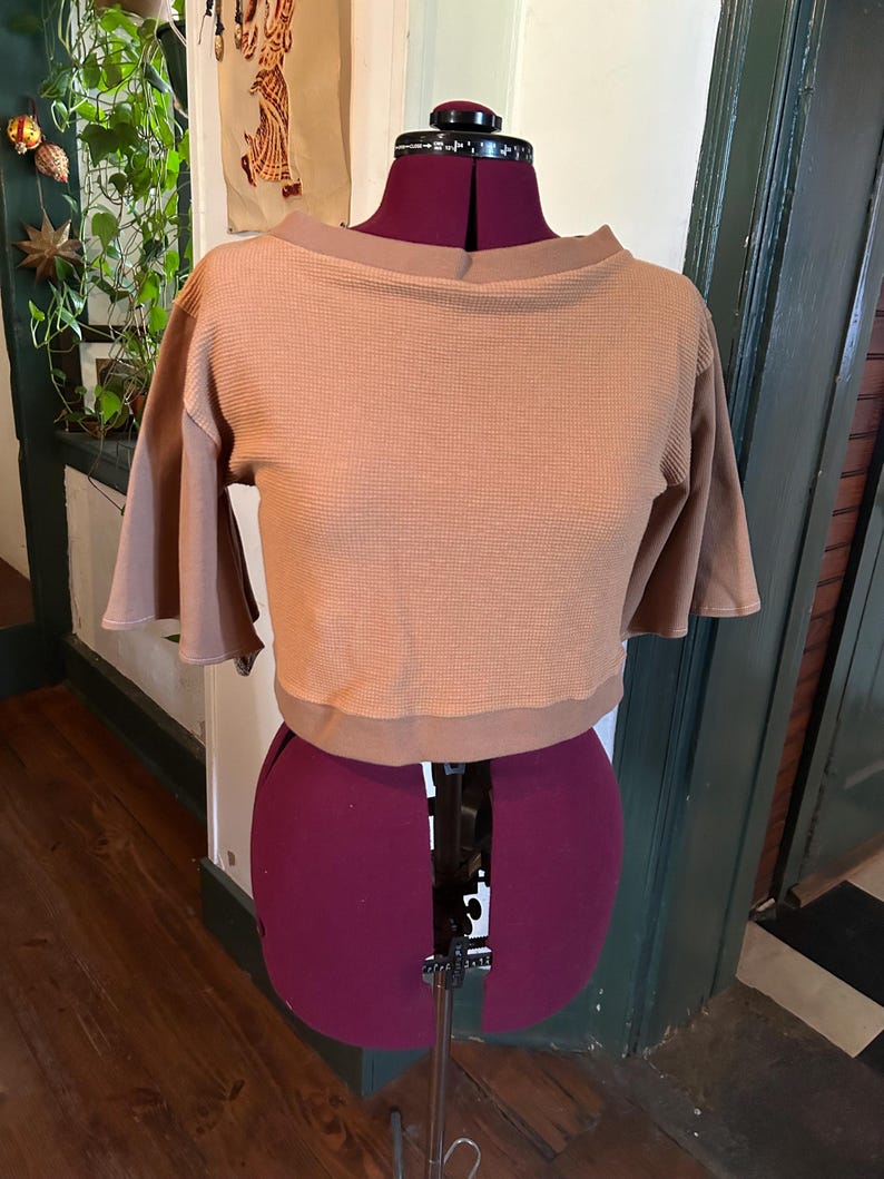 May include: A brown waffle knit cropped top with a boat neck and short sleeves. The top is on a dress form.
