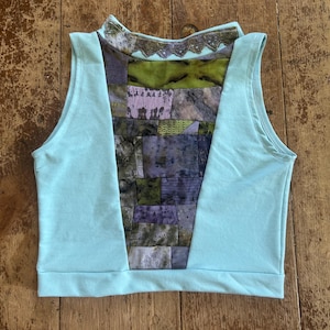 Può includere: Un top corto senza maniche di colore azzurro con un design patchwork. Il patchwork presenta varie tonalità di verde, viola e grigio. Lo scollo è impreziosito da un bordo decorativo. Il top è realizzato in tessuto morbido.