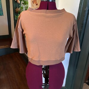 May include: A brown waffle knit cropped top with a boat neck and 3/4 sleeves. The top is on a dress form.