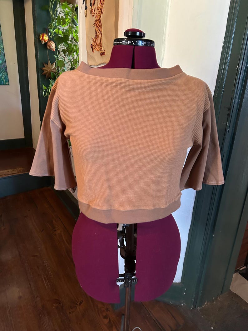May include: A brown waffle knit cropped top with a boat neck and 3/4 sleeves. The top is on a dress form.