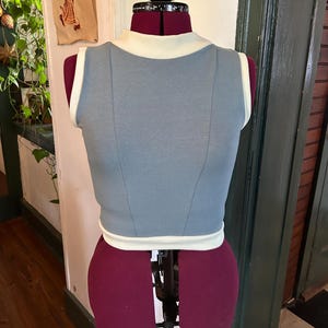May include: A sleeveless, light blue crop top with a white trim around the neck and armholes. The top is made of a soft, stretchy fabric.