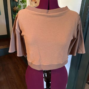 May include: A brown waffle knit cropped top with a boat neck and short sleeves. The top is on a dress form.