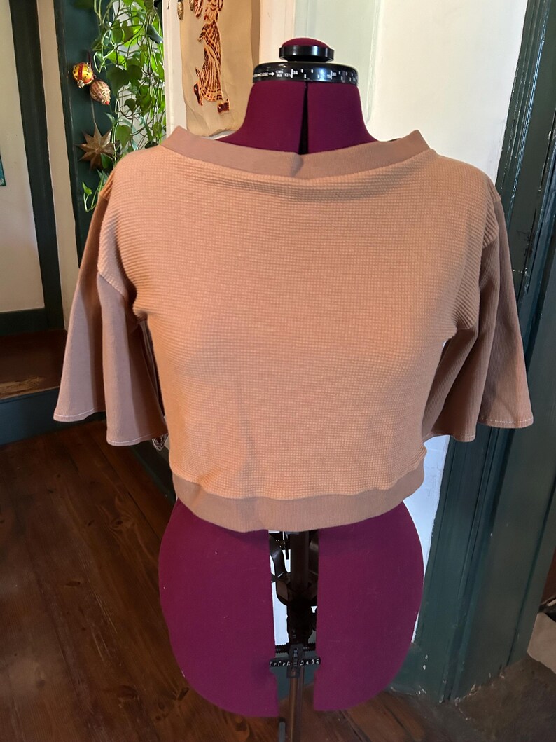 May include: A brown waffle knit cropped top with a boat neck and short sleeves. The top is on a dress form.