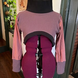 May include: A cropped, long-sleeved shirt with a black turtleneck collar, a pink waffle knit body, and pink long sleeves with black cuffs.