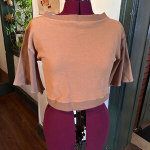 May include: A brown waffle knit cropped top with a boat neck and short sleeves. The top is on a dress form.