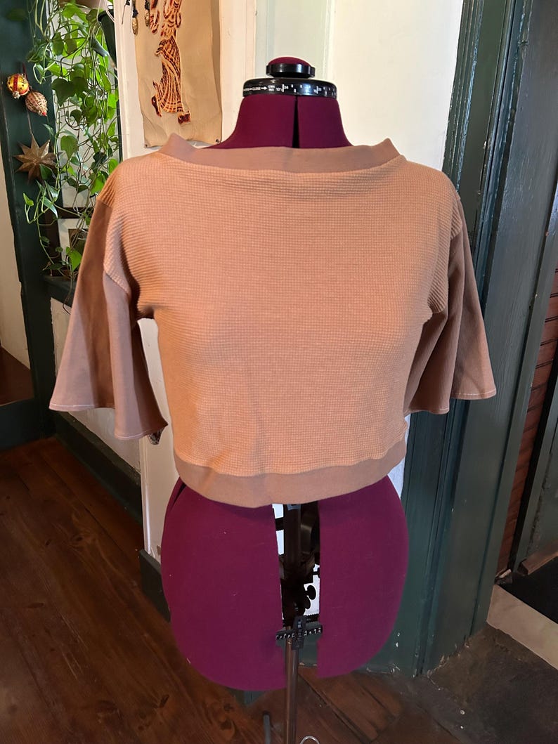 May include: A brown waffle knit cropped top with a boat neck and short sleeves. The top is on a dress form.