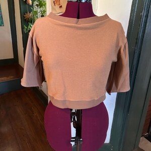 May include: A brown waffle knit cropped top with a boat neck and 3/4 sleeves. The top is on a dress form.