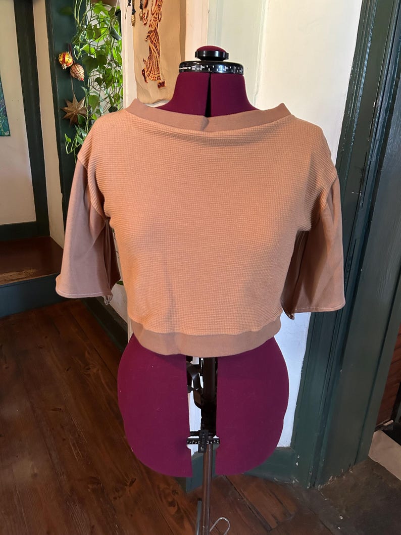 May include: A brown waffle knit cropped top with a boat neck and 3/4 sleeves. The top is on a dress form.
