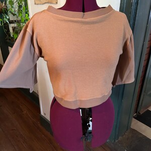 May include: A brown waffle knit cropped top with a boat neck and 3/4 sleeves. The top is on a dress form.