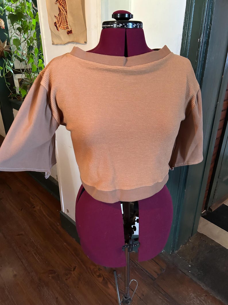 May include: A brown waffle knit cropped top with a boat neck and 3/4 sleeves. The top is on a dress form.