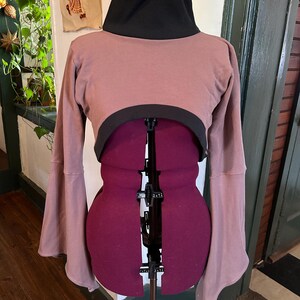 May include: A mauve cropped sweater with a black turtleneck and long bell sleeves.