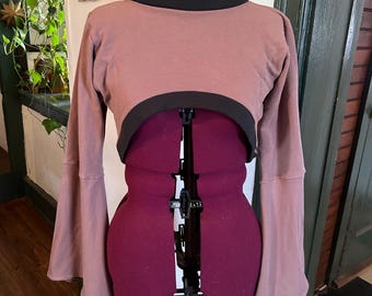 May include: A mauve cropped sweater with a black turtleneck and long bell sleeves.