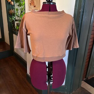 May include: A brown waffle knit cropped top with a boat neck and short sleeves. The top is on a dress form.
