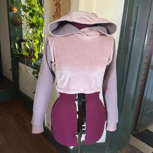 May include: A pink and gray cropped hoodie with a waffle knit fabric on the sleeves and a velour fabric on the body and hood.