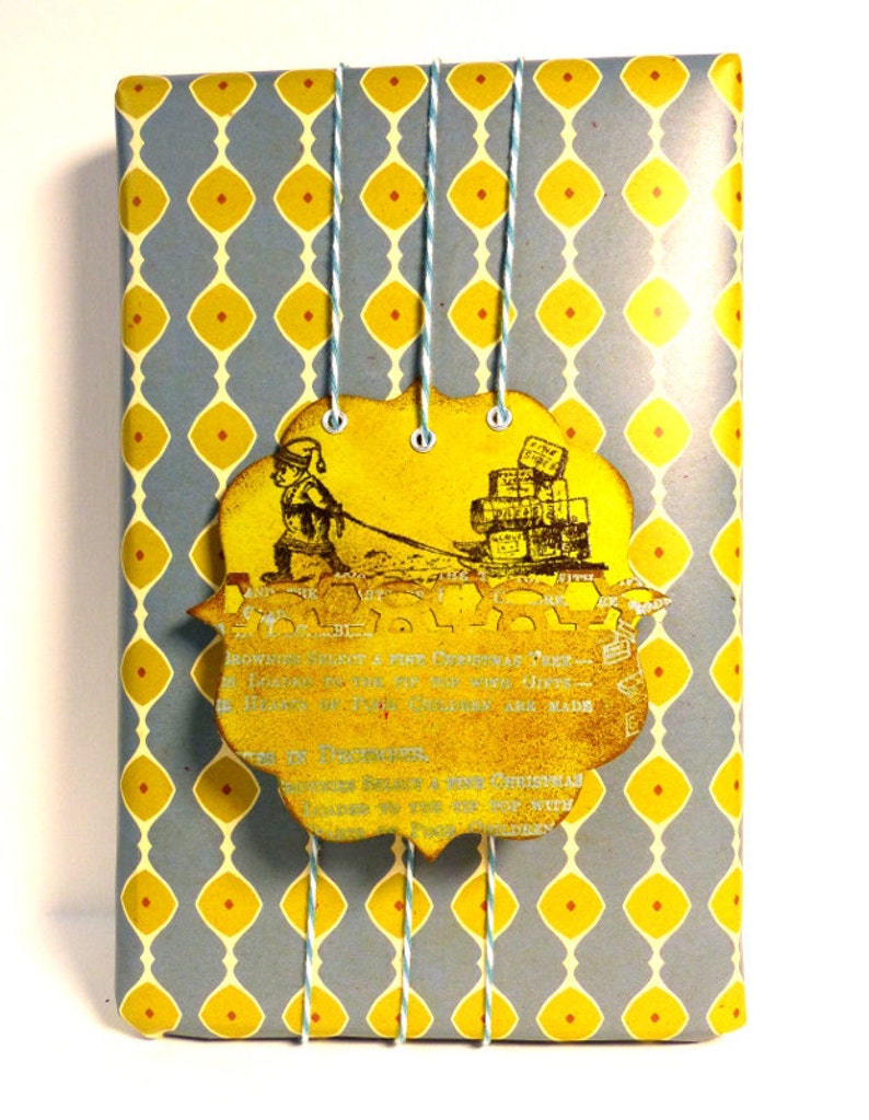 May include: A blue and yellow patterned gift wrap with a yellow tag attached. The tag features a vintage illustration of a person pulling a sled full of gifts. The tag also includes text that reads "Brownies sold for a fine Christmas Tree - London to the Bay and everywhere - Heaven's 1st Enchantments are made in December - We'd rather believe a fine Christmas because we are too old for wishing upon the top but with every wish we make we hope it will come true."