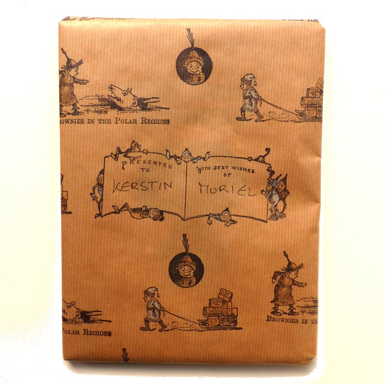 May include: Brown wrapping paper with a repeating pattern of small illustrations of people and objects. The paper has a handwritten inscription that reads "Presented to Kerstin with best wishes of Muriel".