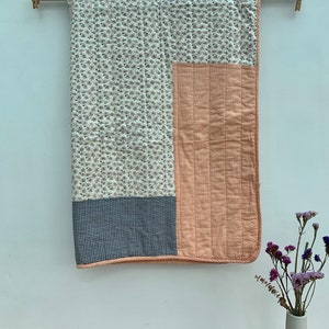 May include: A patchwork quilt with a floral print, orange and white gingham, and blue and white gingham. The quilt is hanging on a wooden rod against a white wall.