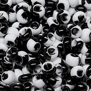 May include: A close-up shot of a pile of black and white beads. The beads are cylindrical with a hole running through the center. Each bead is half black and half white, creating a striking contrast. The beads are scattered, filling the frame.