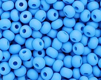 Puede incluir: Una gran colección de pequeñas cuentas redondas de color azul claro con acabado mate. Cada cuenta presenta una superficie lisa y opaca con un orificio central para enhebrar. Las cuentas están densamente agrupadas, creando una textura uniforme.