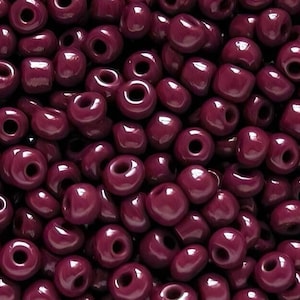 May include: A close-up view of a large quantity of small, round, dark purple beads. The beads are all the same size and shape, and they are arranged in a random pattern.