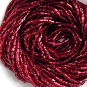 May include: A close-up of a strand of red glass seed beads. The beads are small and cylindrical, with a shiny, metallic finish.