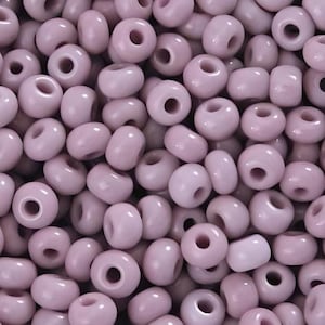 May include: A large pile of small, round, light purple glass beads. The beads are all the same size and shape, and they are arranged in a random pattern.