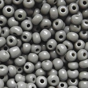 May include: A large pile of gray glass seed beads. The beads are round and have a hole in the center.