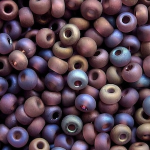 May include: A close-up of a large pile of iridescent glass beads in shades of purple, brown, and blue. The beads are small and round, with a smooth, matte finish.