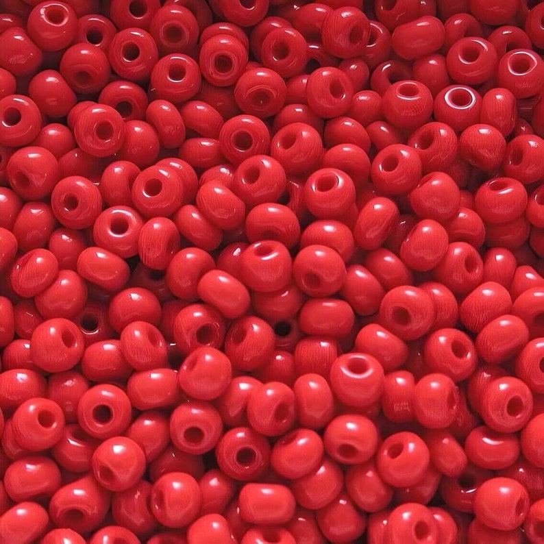 May include: A close-up image of a large quantity of small, red, round seed beads. The beads are arranged in a random pattern, creating a textured surface.