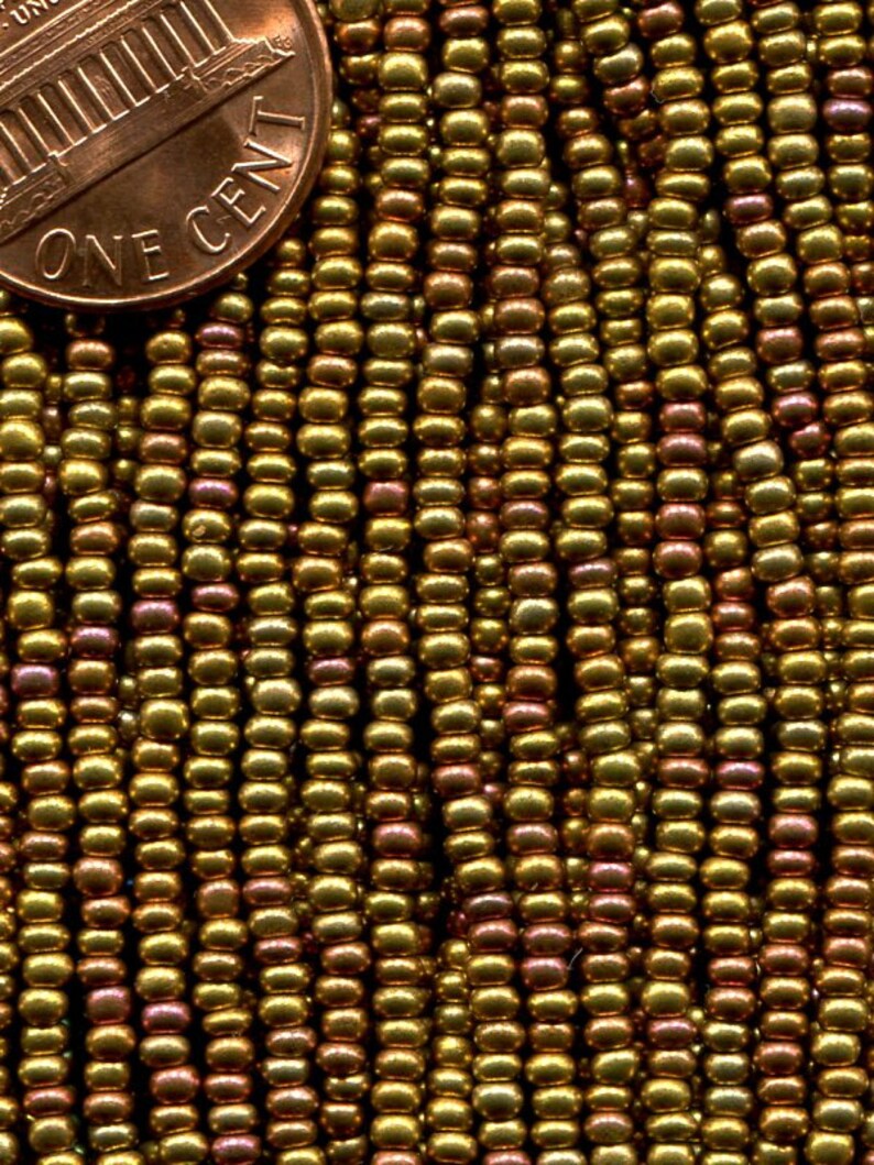 Puede incluir: Primer plano de una hebra de peque&ntilde;as cuentas doradas con un ligero brillo iridiscente. Las cuentas est&aacute;n dispuestas en filas y tienen aproximadamente el tama&ntilde;o de una moneda de un c&eacute;ntimo de euro.