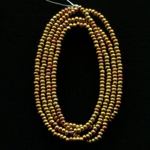 Puede incluir: Una hebra de cuentas de color dorado y cobre, dispuestas en c&iacute;rculo.
