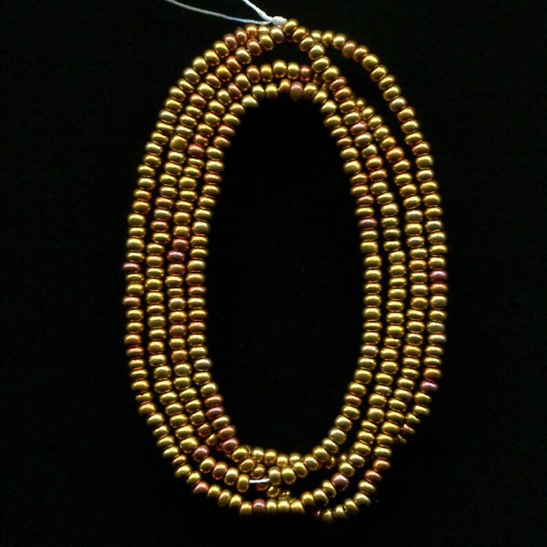 Puede incluir: Una hebra de cuentas de color dorado y cobre, dispuestas en c&iacute;rculo.
