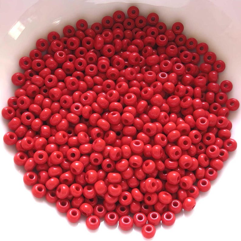 May include: A large quantity of small, round, red beads. The beads are all the same size and shape, and they are arranged in a random pattern.