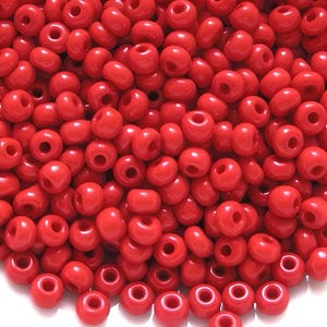May include: A close-up image of a large quantity of small, round, red beads. The beads are made of glass and have a smooth, shiny finish.