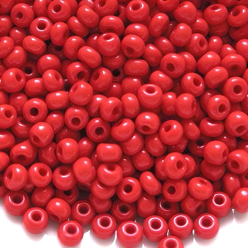 May include: A close-up image of a large quantity of small, round, red beads. The beads are made of glass and have a smooth, shiny finish.