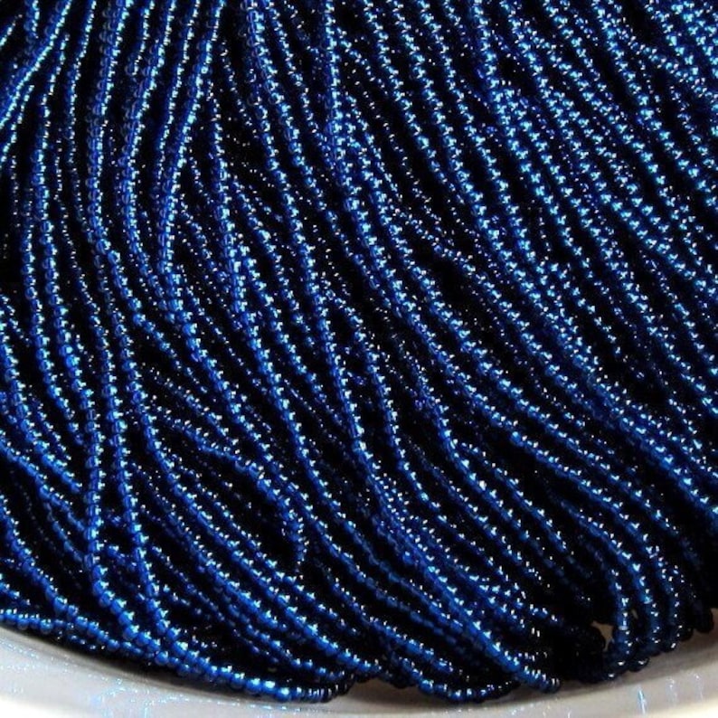 Op de afbeelding: Een close-up van een stapel donkerblauwe kralen. De kralen zijn klein en rond en hebben een metallic glans.