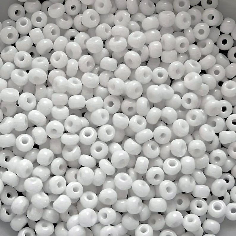 May include: A large quantity of white seed beads. The beads are small and round, with a hole in the center. They are perfect for crafting and jewelry making.