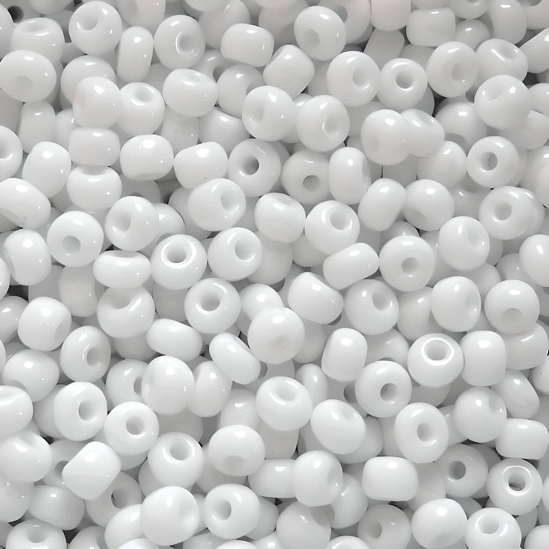 May include: A close-up image of a large quantity of white seed beads. The beads are round and have a small hole in the center.