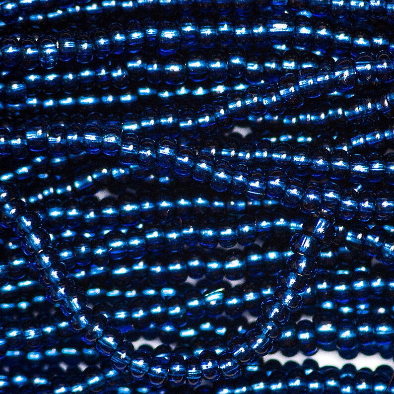 Op de afbeelding: Een close-up van een stapel donkerblauwe glazen kralen. De kralen zijn klein en rond en hebben een glanzende, metallic afwerking.