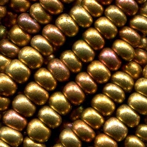 Puede incluir: Primer plano de un grupo de peque&ntilde;as cuentas redondas de color dorado con un brillo met&aacute;lico. Las cuentas est&aacute;n dispuestas en un patr&oacute;n escalonado, creando una superficie texturizada.