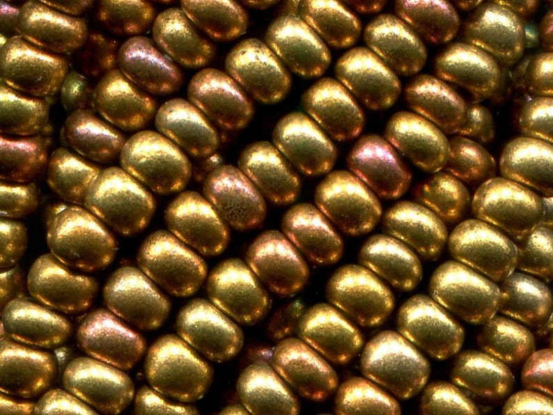 Puede incluir: Primer plano de un grupo de peque&ntilde;as cuentas redondas de color dorado con un brillo met&aacute;lico. Las cuentas est&aacute;n dispuestas en un patr&oacute;n escalonado, creando una superficie texturizada.