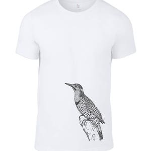May include: White t-shirt with a black and white illustration of a woodpecker perched on a branch.