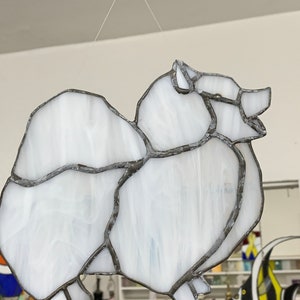 May include: A white stained glass Pomeranian dog hanging from a string. The dog is made of white glass with black outlines.