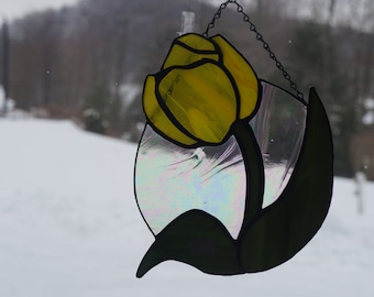 May include: A stained glass window hanging featuring a yellow tulip flower design. The tulip is surrounded by a clear iridescent glass background.
