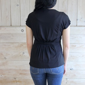 Puede incluir: Una camisa negra de manga corta con cintura ajustada y cuello redondo. La camisa se lleva con pantalones vaqueros azules.