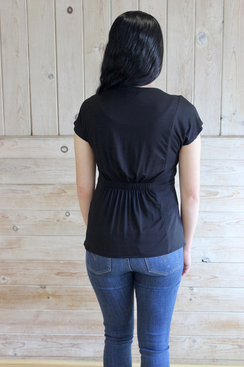 Puede incluir: Una camisa negra de manga corta con cintura ajustada y cuello redondo. La camisa se lleva con pantalones vaqueros azules.