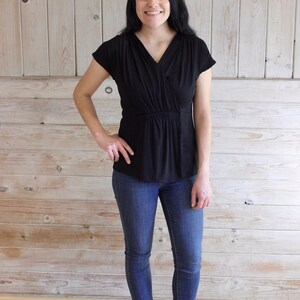 Puede incluir: Una mujer con un top negro de manga corta con cuello en V y cintura fruncida, jeans azules y botines marrones.