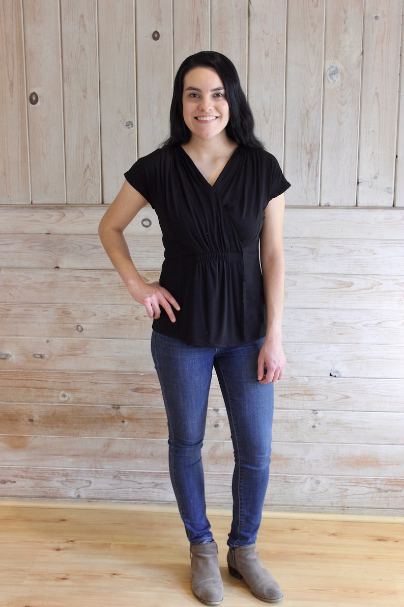 Puede incluir: Una mujer con un top negro de manga corta con cuello en V y cintura fruncida, jeans azules y botines marrones.